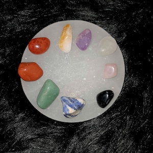 May include: A white circular tray with 10 different colored stones arranged in a circle. The stones are various shades of red, orange, yellow, green, blue, purple, pink, white, and black.