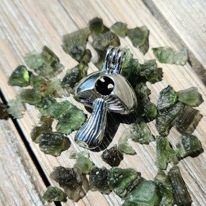 May include: A silver mushroom charm with a hollow center, surrounded by small green crystals.