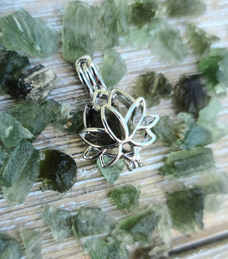 May include: Silver lotus flower charm with a delicate design. The charm is surrounded by small green stones.