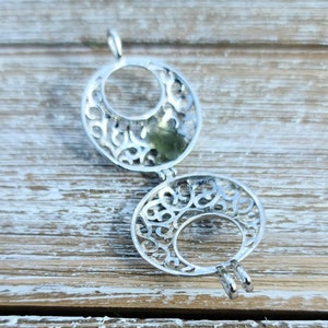 May include: Silver filigree charm with a circular design. The charm is open and has a delicate, intricate pattern.