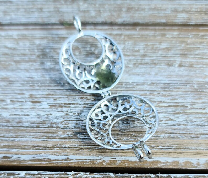 May include: Silver filigree charm with a circular design. The charm is open and has a delicate, intricate pattern.