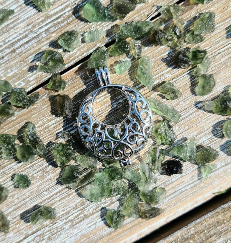 May include: A silver filigree cage pendant with a delicate, intricate design. The pendant is surrounded by small, green, translucent stones.