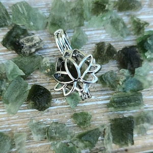 May include: Silver lotus flower charm pendant with a delicate openwork design. The charm is surrounded by small green crystals.