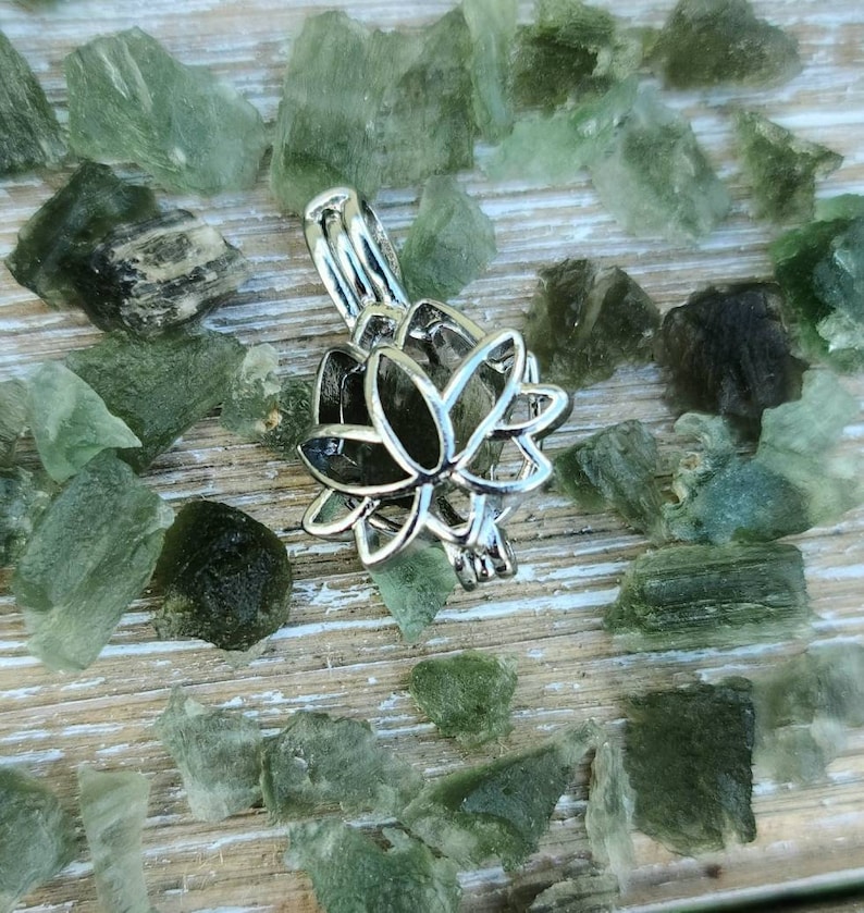 May include: Silver lotus flower charm pendant with a delicate openwork design. The charm is surrounded by small green crystals.