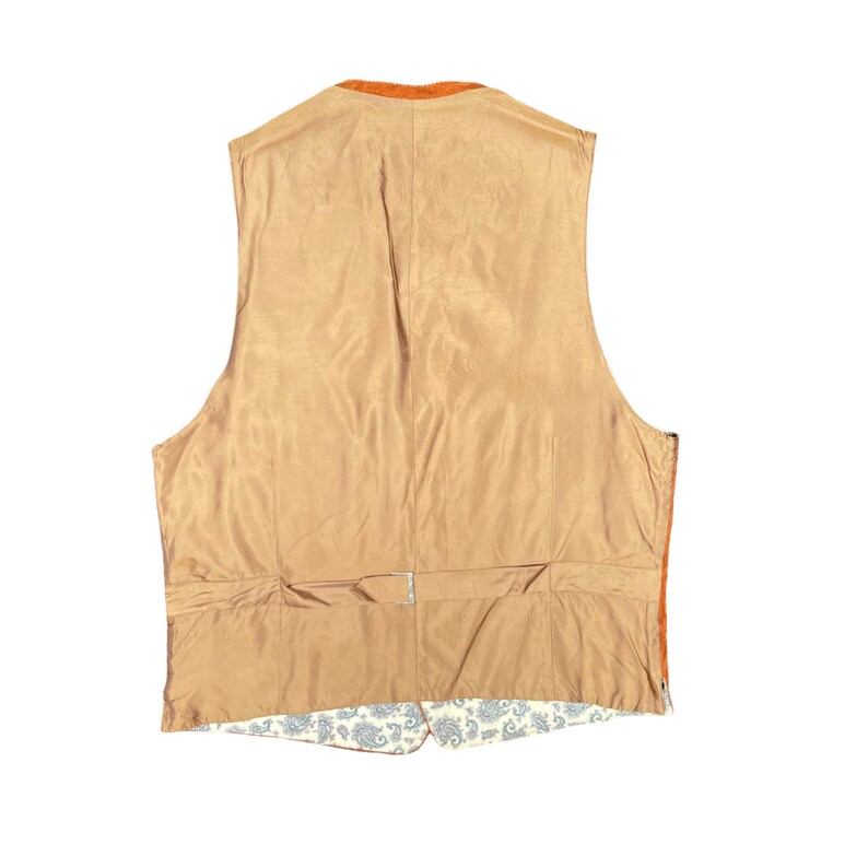 May include: Back view of a brown vest with an orange collar. The vest has a satin-like lining and a paisley patterned bottom. A silver buckle is visible at the back waist. The vest is a classic style.