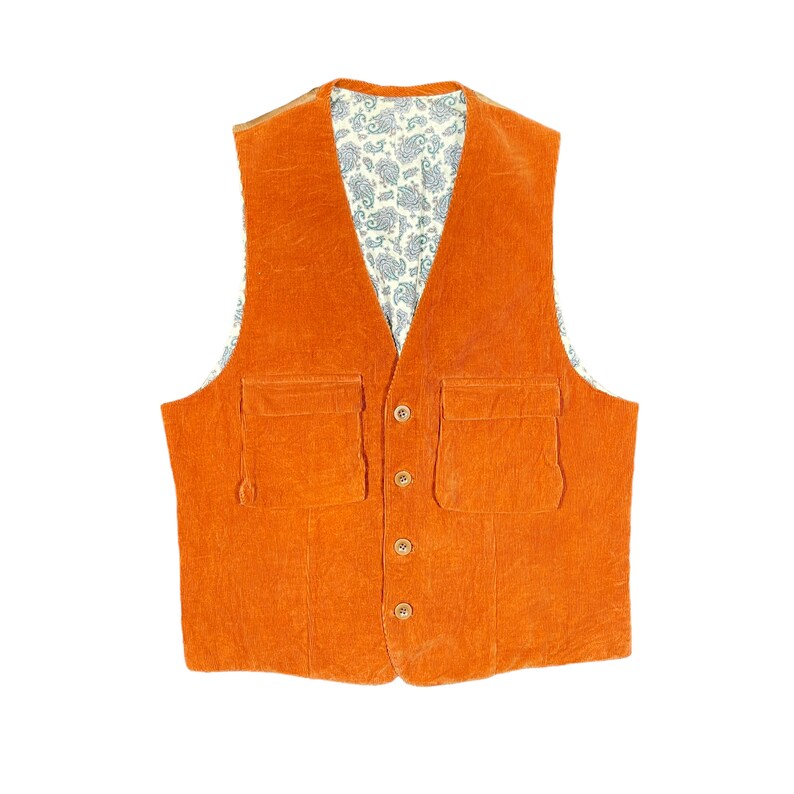 May include: An orange corduroy vest with two front pockets and wooden buttons. The vest's interior lining features a paisley pattern in shades of blue and white. A classic garment for layering.