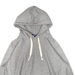 K&ouml;nnte beinhalten: Ein melierter grauer Kapuzenpullover mit Kapuze und Kordelzug sowie wei&szlig;en Kordeln. Das Sweatshirt hat eine K&auml;ngurutasche. Der Stoff scheint ein weiches, bequemes Material zu sein, das sich f&uuml;r Freizeitkleidung eignet. Der Hoodie ist ein klassisches, vielseitiges Kleidungsst&uuml;ck.