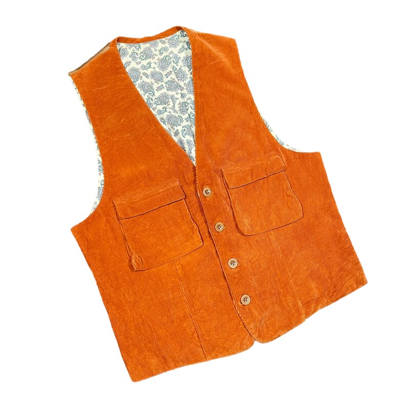 May include: An orange corduroy vest with two front pockets and wooden buttons. The vest's interior lining features a paisley pattern in white and blue. The vest is a classic style.