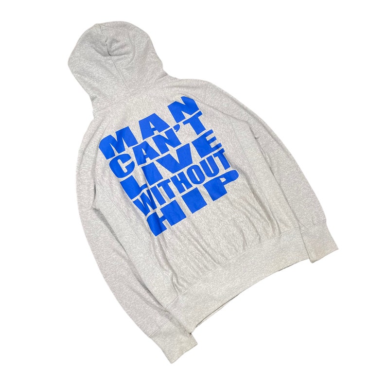 K&ouml;nnte beinhalten: Ein hellgrauer Kapuzenpullover mit langen &Auml;rmeln. Auf der R&uuml;ckseite steht in blauer Schrift "MAN CAN'T LIVE WITHOUT HIP". Der Pullover besteht aus einem weichen, bequemen Material.