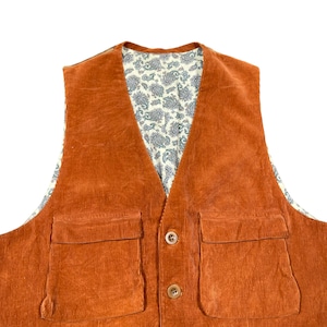 May include: An orange corduroy vest with two front pockets and two brown buttons. The interior lining features a cream-colored paisley pattern with blue and green accents. The vest is a classic style.