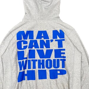 K&ouml;nnte beinhalten: Hellgrauer Kapuzenpullover mit Kapuze. Auf der R&uuml;ckseite des Hoodies steht in blauer Schrift "MAN CAN'T LIVE WITHOUT HIP". Der Hoodie besteht aus einem weichen, bequemen Material.