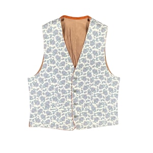 May include: A cream-colored vest with a paisley pattern in shades of blue and green. The vest has a brown lining and trim, with four buttons down the front. A classic, tailored garment.