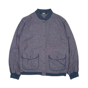 Op de afbeelding: Blauwe bomberjack met een geweven textuur. De jas heeft een knoopsluiting, twee voorzakken en een geribbelde kraag en manchetten. De afwerking van de jas is een donkerdere blauwtint.