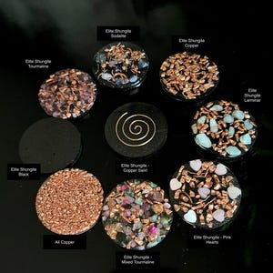 May include: A collection of Elite Shungite stones with various designs and materials. The stones include copper, tourmaline, sodalite, and pink hearts. Each stone is round and has a unique pattern, with text labels identifying each type.