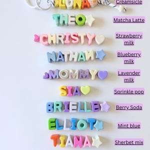Op de afbeelding: Een collectie gepersonaliseerde sleutelhangers en naamplaatjes van siliconen kralen met verschillende kleurthema's, gelabeld als Creamsicle, Matcha Latte, Strawberry milk, Blueberry milk, Lavender milk, Sprinkle pop, Berry Soda, Mint blue, Sherbet mix en Super Pop.