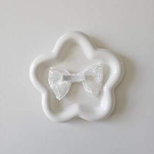 May include: A white ceramic star-shaped dish with a white lace bow in the center.