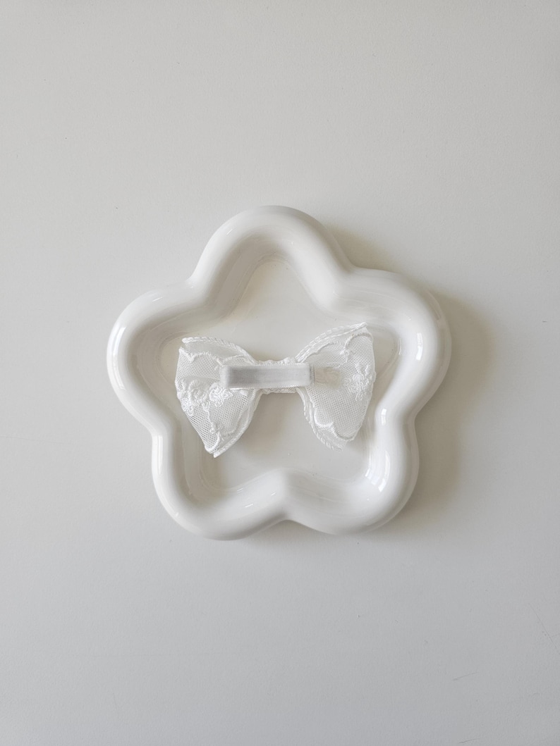 May include: A white ceramic star-shaped dish with a white lace bow in the center.