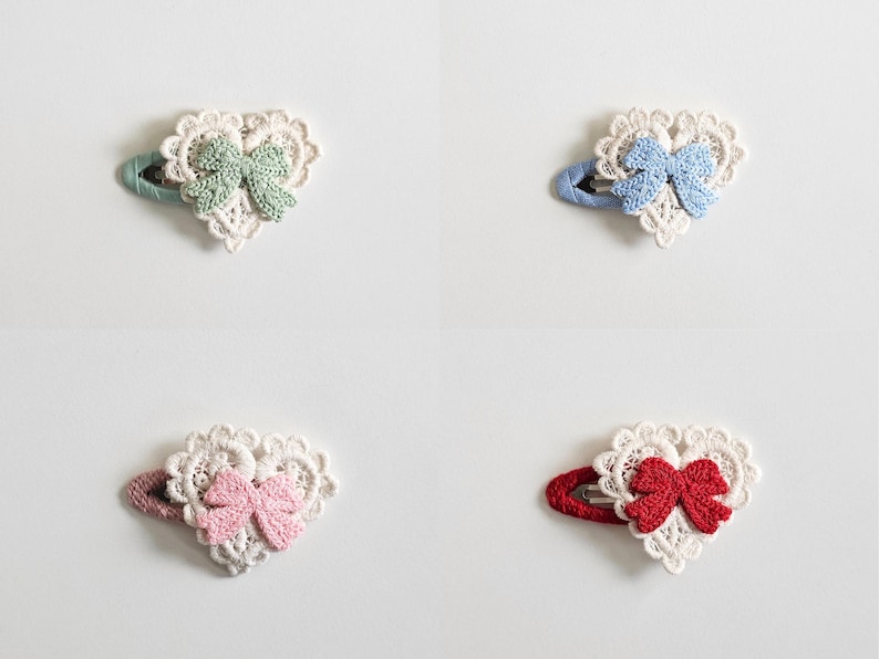 Pu&ograve; includere: Quattro fermagli per capelli a forma di cuore con dettagli in pizzo e un fiocco. Ogni fermaglio presenta un fiocco di colore diverso: verde, blu, rosa e rosso. I fermagli sono su sfondo bianco.