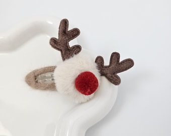 Puede incluir: Pinza para el pelo con forma de reno. Presenta una cabeza blanca y esponjosa, una nariz de pompón rojo y cuernos de fieltro marrón. El clip es de metal plateado. Un divertido accesorio para las fiestas navideñas.