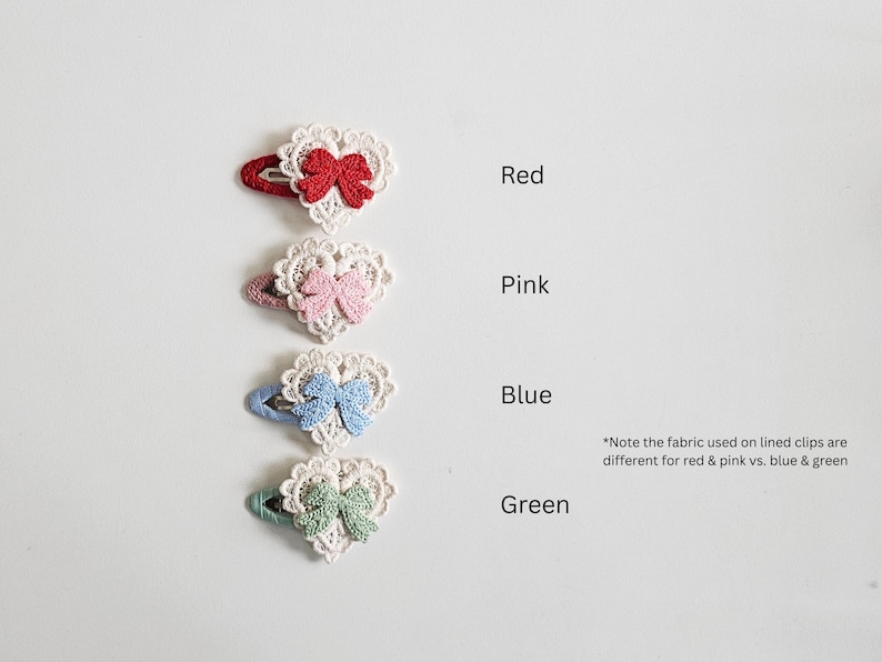 Pu&ograve; includere: Quattro fermagli per capelli a forma di cuore rossi, rosa, blu e verdi. Ogni fermaglio presenta un cuore di pizzo bianco con un fiocco abbinato. Il testo indica i colori.