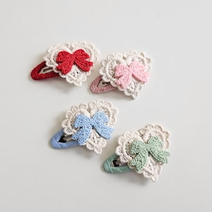 Pu&ograve; includere: Quattro fermagli per capelli a forma di cuore con pizzo all'uncinetto e fiocchi. I fiocchi sono rossi, rosa, blu e verdi. Le clip sono in vari colori, tra cui rosso, rosa, blu e verde. Gli accessori per capelli sono su sfondo bianco.