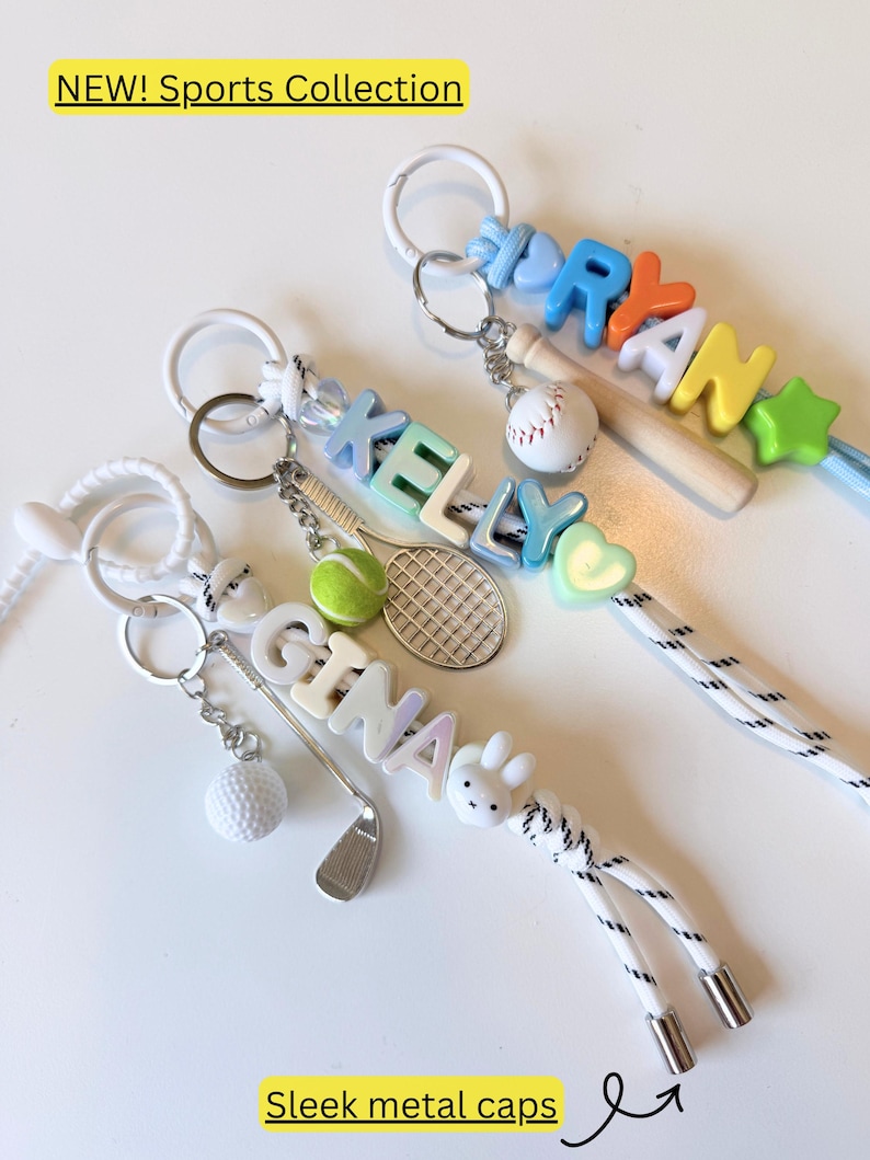 Op de afbeelding: Drie gepersonaliseerde sleutelhangers met witte koorden en metalen uiteinden. E&eacute;n toont de naam GINA met een golfclub en balbedel. Een andere toont KELLY met een tennisracket en balbedel. De derde toont RYAN met een honkbalknuppel en balbedel.