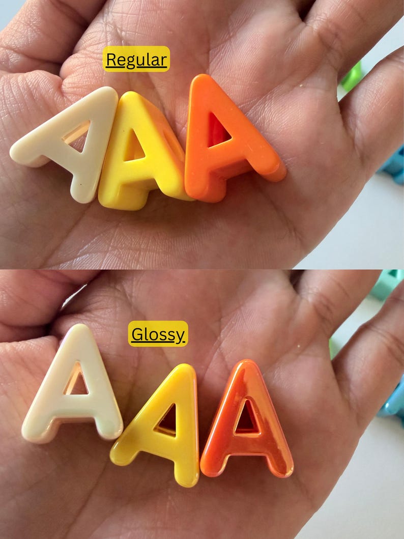 Op de afbeelding: Drie letter A-vormen in cr&egrave;me, geel en oranje. Het bovenste gedeelte toont de letters met een normale afwerking, terwijl het onderste gedeelte dezelfde letters met een glanzende afwerking laat zien. Elke letter is een solide, driedimensionaal object.