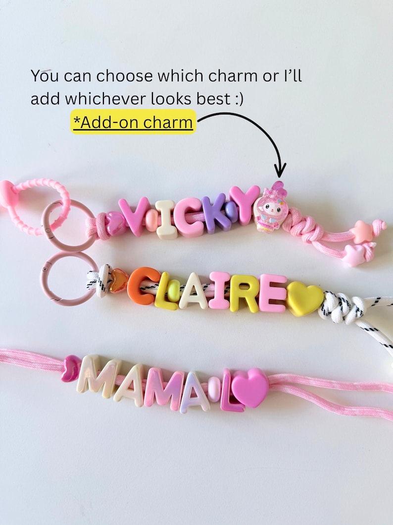 Op de afbeelding: Drie gepersonaliseerde kralenkoorden met kleurrijke letterkralen die VICKY, CLAIRE en MAMA spellen. De koorden bevatten roze en witte touwtjes, hartvormige kralen en een kleine figuurbedel. Tekst: You can choose which charm or I&rsquo;ll add whichever looks best :) *Add-on charm.