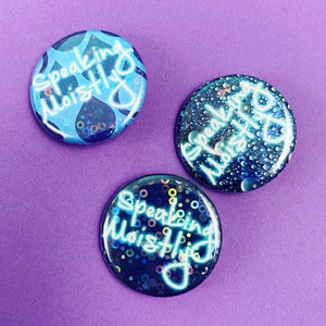 May include: Three round blue and black buttons with the text "Speaking Moistly" in white neon lettering. The buttons have different designs, one with blue water droplets, one with blue and black glitter, and one with blue and black water droplets.