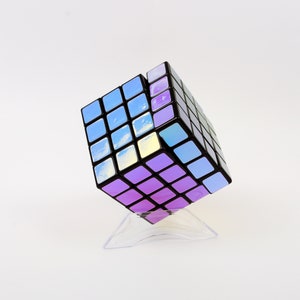 以下が含まれることがあります： 虹色のステッカーが付いた黒と紫の3x3ルービックキューブパズル。キューブは透明なプラスチックスタンドの上に置かれています。