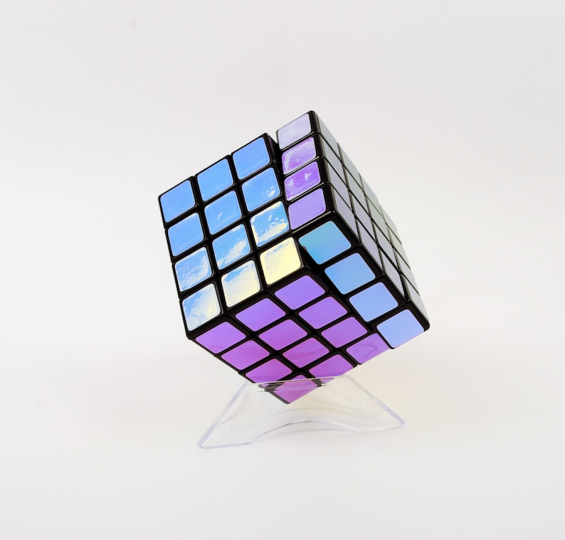 以下が含まれることがあります： 虹色のステッカーが付いた黒と紫の3x3ルービックキューブパズル。キューブは透明なプラスチックスタンドの上に置かれています。