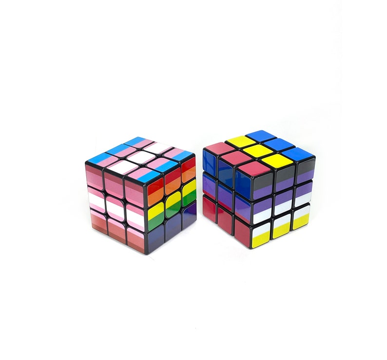 May include: Two 3x3 Rubik's Cubes with different flag designs. One cube has the transgender pride flag and the other has the Ukrainian flag.