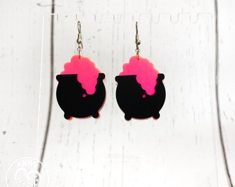 May include: A pair of black and pink cauldron earrings. The cauldrons are filled with pink bubbling liquid.