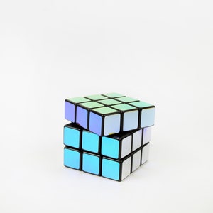 以下が含まれることがあります： 虹色のステッカーが付いた黒と白のルービックキューブ。キューブは部分的に解かれており、一部のステッカーは正しい位置にあります。
