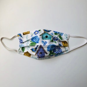 May include: White face mask with a blue and green floral pattern featuring birdhouses and birds.