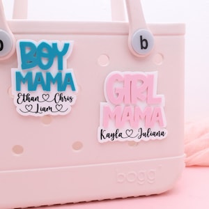 May include: A light pink tote bag with two decorative stickers. One sticker reads "BOY MAMA" in blue with the names Ethan, Chris, and Liam. The other sticker says "GIRL MAMA" in pink with the names Kayla and Juliana.