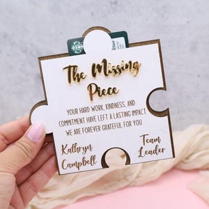 May include: A wooden puzzle piece with the words "The Missing Piece" in gold lettering. The text below reads "Your hard work, kindness, and commitment have left a lasting impact. We are forever grateful for you." A gift card is inserted.