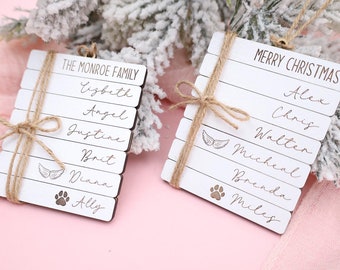 May include: Two white wooden Christmas ornaments with names and a paw print or angel wings. The ornament on the left says "The Monroe Family" with the names Elizabeth, Angel, Justine, Brit, Diana, and Ally. The ornament on the right says "Merry Christmas" with the names Alex, Chris, Walter, Micheal, Brenda, and Miles.