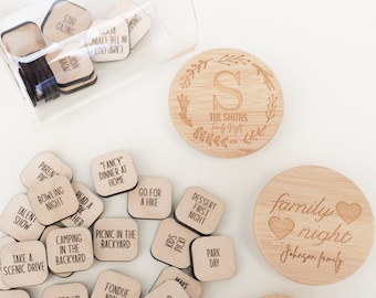 May include: A set of wooden family night activity ideas in a glass jar with a wooden lid. The lid has the text "The Smiths Family Night" and a letter S. The jar contains small wooden squares with different activities written on them, such as "Camping in the Backyard", "Try a New Restaurant", and "Dance Party".