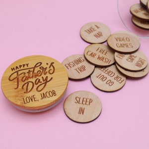 May include: A wooden jar with a lid that says "Happy Father's Day Love, Jacob". The jar is filled with small wooden circles, each with a different activity written on it, such as "Take a Nap", "Free Car Wash", "Fishing Trip", and "Sleep In".