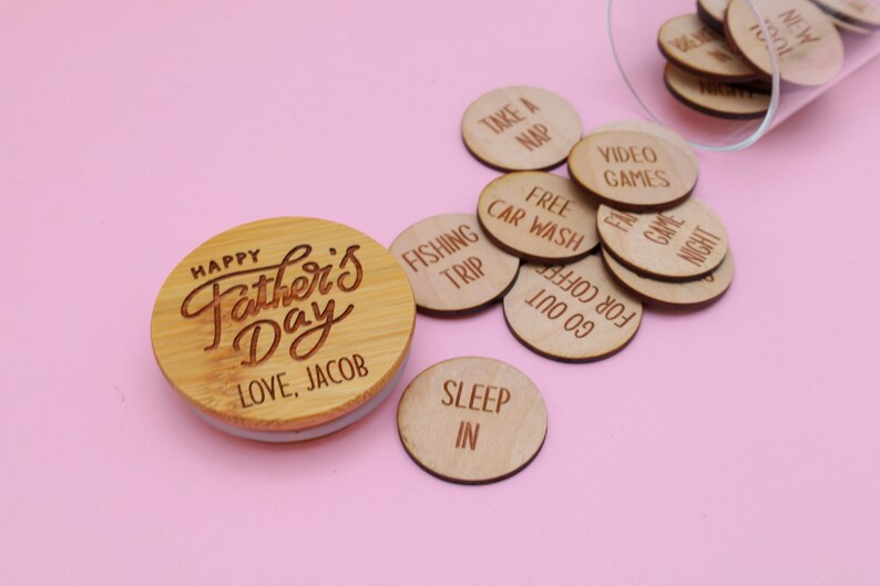 May include: A wooden jar with a lid that says "Happy Father's Day Love, Jacob". The jar is filled with small wooden circles, each with a different activity written on it, such as "Take a Nap", "Free Car Wash", "Fishing Trip", and "Sleep In".