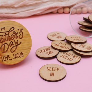 May include: A wooden round disc with the text "Happy Father's Day Love, Jacob" engraved on it. A glass jar filled with small wooden discs with various phrases like "Take a Nap", "Free Car Wash", "Fishing Trip", "Go for Coffee", "Sleep In", and "Video Games" is next to the disc.