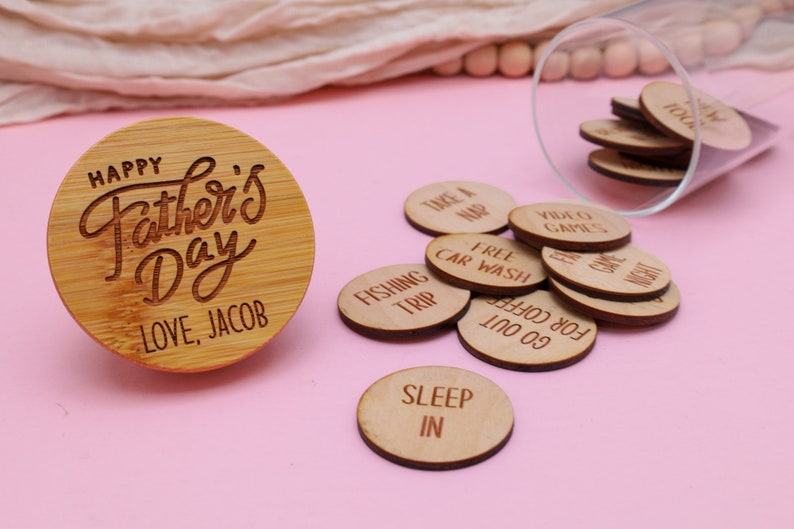 May include: A wooden round disc with the text "Happy Father's Day Love, Jacob" engraved on it. A glass jar filled with small wooden discs with various phrases like "Take a Nap", "Free Car Wash", "Fishing Trip", "Go for Coffee", "Sleep In", and "Video Games" is next to the disc.