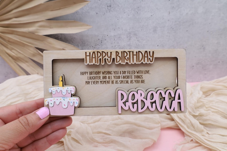 Puede incluir: Una tarjeta de cumplea&ntilde;os de madera con un pastel rosa y el texto "HAPPY BIRTHDAY! WISHING YOU A DAY FILLED WITH LOVE LAUGHTER, AND ALL YOUR FAVORITE THINGS MAY EVERY MOMENT BE AS SPECIAL AS YOU ARE REBECCA"