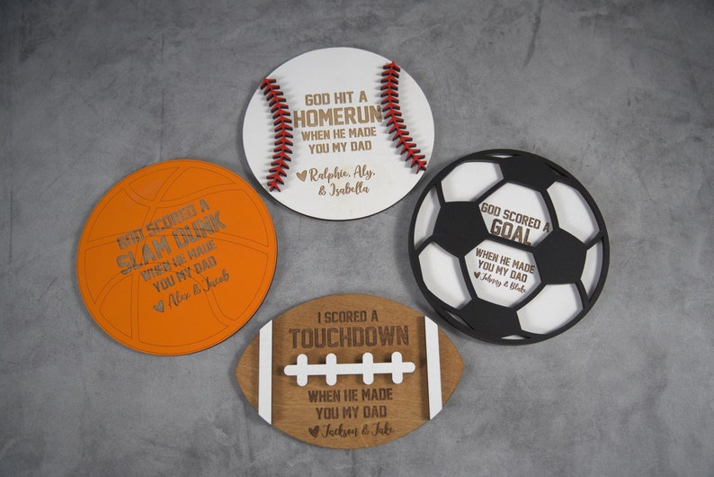 May include: Four wooden plaques shaped like different sports balls. Each plaque has a sports-themed message and a personalized name. The plaques are on a gray background.