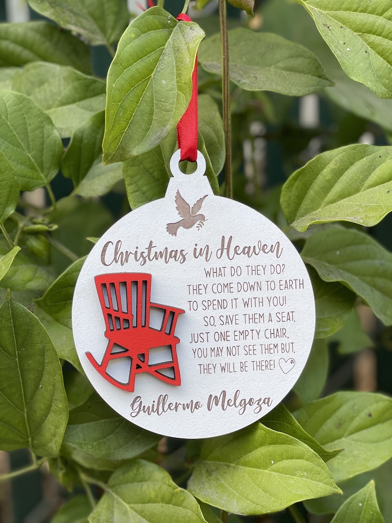 May include: White wooden Christmas ornament with a red rocking chair and the text "Christmas in Heaven" and "Guillermo Melgoza". The ornament has a dove with an olive branch in its beak.