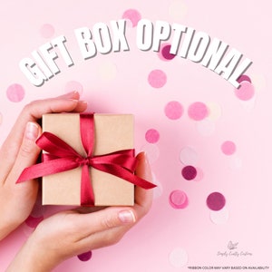 May include: A brown gift box with a red ribbon tied in a bow. The box is being held by two hands against a pink background with confetti.