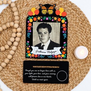 May include: A black memorial frame featuring a monarch butterfly, colorful floral accents, and a black and white portrait of a man named Guillermo Melgoza. Below, a black rectangular base displays the text: Though you are no longer here with us, your light, your love, and your memory will forever live in our hearts. Until we meet again.