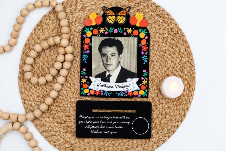 May include: A black memorial frame featuring a monarch butterfly, colorful floral accents, and a black and white portrait of a man named Guillermo Melgoza. Below, a black rectangular base displays the text: Though you are no longer here with us, your light, your love, and your memory will forever live in our hearts. Until we meet again.
