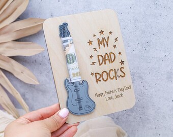 May include: A wooden Father's Day card with a guitar-shaped money holder. The card reads "My Dad Rocks" with a guitar graphic and a rolled-up bill. The message "Happy Father's Day Dad, Love, Jacob" is also included.